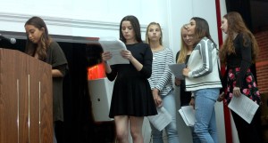 A photo of myself, Avery Kutis, telling my personal story (far left), while Caroline Loeb (left), Stella-Rose Gahan (middle left), Alexa Code (middle back), Nathalie Friedman (middle right), and E Jeremijenko-Conley (far right) read along during our International Day of the Girl assembly (photo credit: Steve ?)